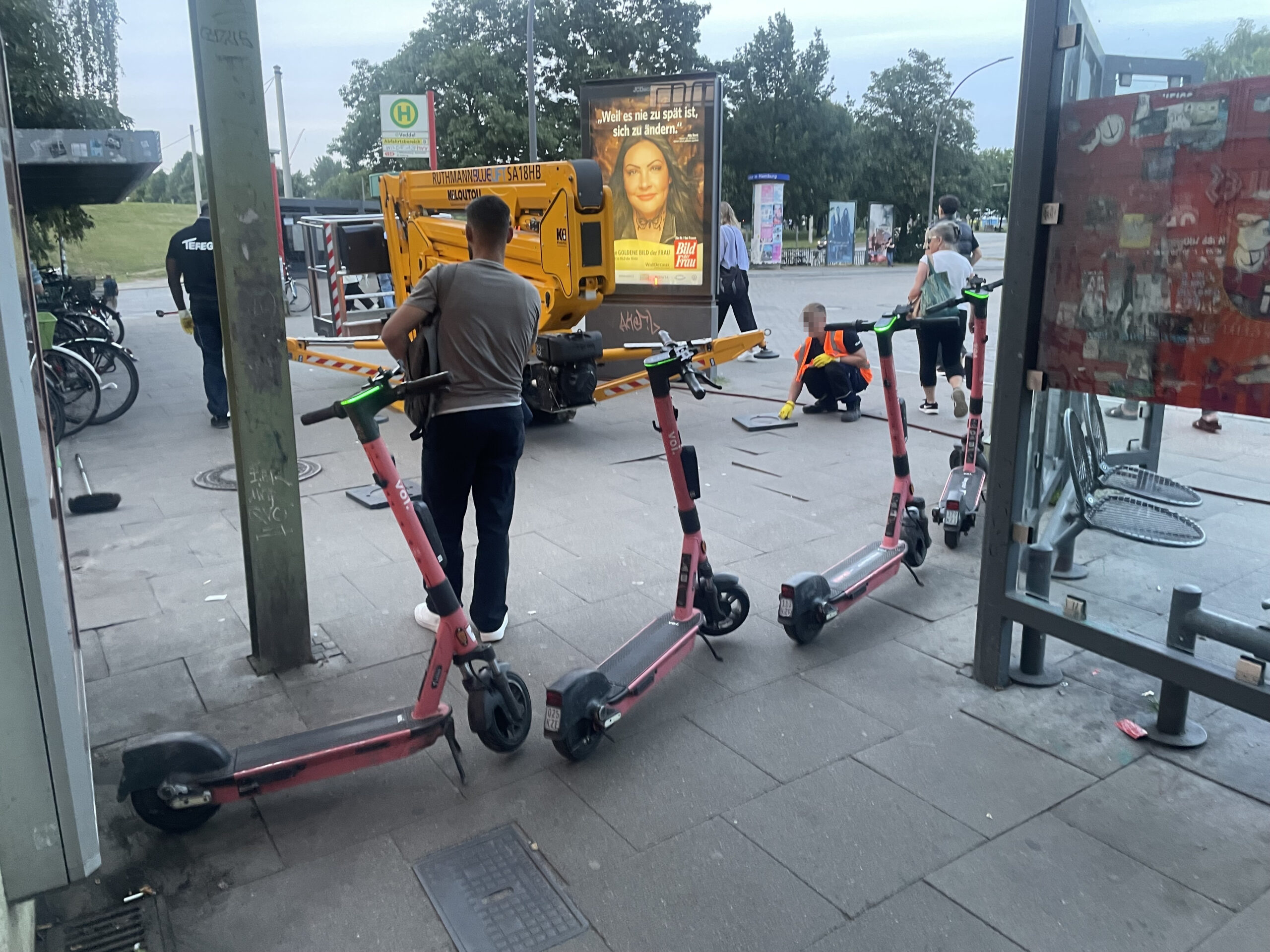 Eine Viererkette Voi-Roller versperrt Pendlern den Durchgang. Dahinter bauen Mitarbeiter der Hochbahn-Dienstleister „Tereg“ eine Arbeitsbühne auf. Alles nur ein Zufall, meint die Hochbahn.