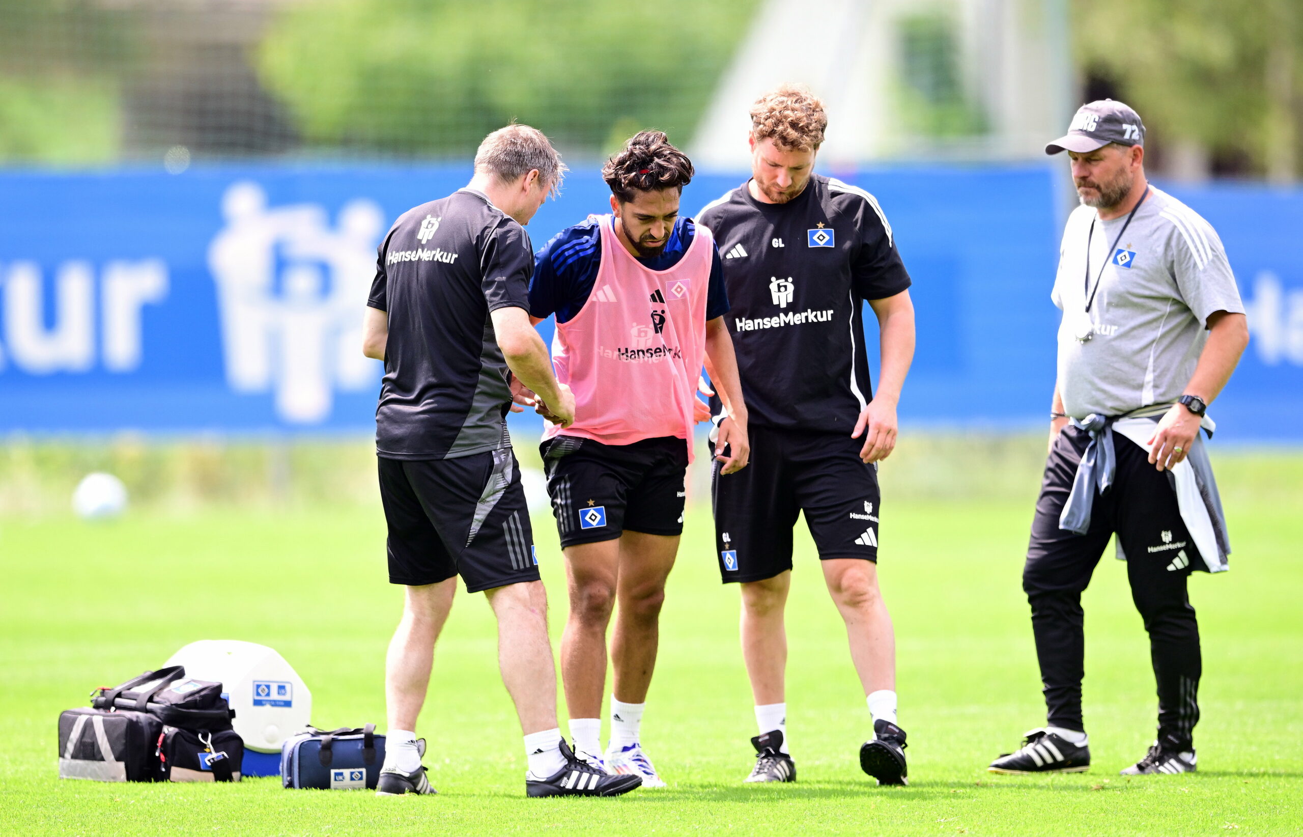 Immanuel Pherai humpelt mit schmerzverzerrtem Gesicht über den Trainingsplatz, wird dabei gestützt von Mannschaftsarzt Dr. Wolfgang Schillings (l.) und Physiotherapeut Gerrit Lüders (3.v.l.)