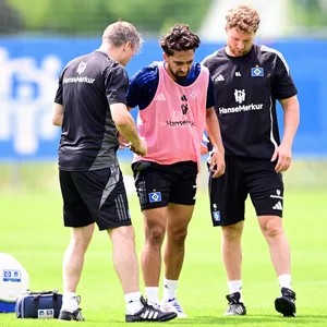 Immanuel Pherai humpelt mit schmerzverzerrtem Gesicht über den Trainingsplatz, wird dabei gestützt von Mannschaftsarzt Dr. Wolfgang Schillings (l.) und Physiotherapeut Gerrit Lüders (3.v.l.)