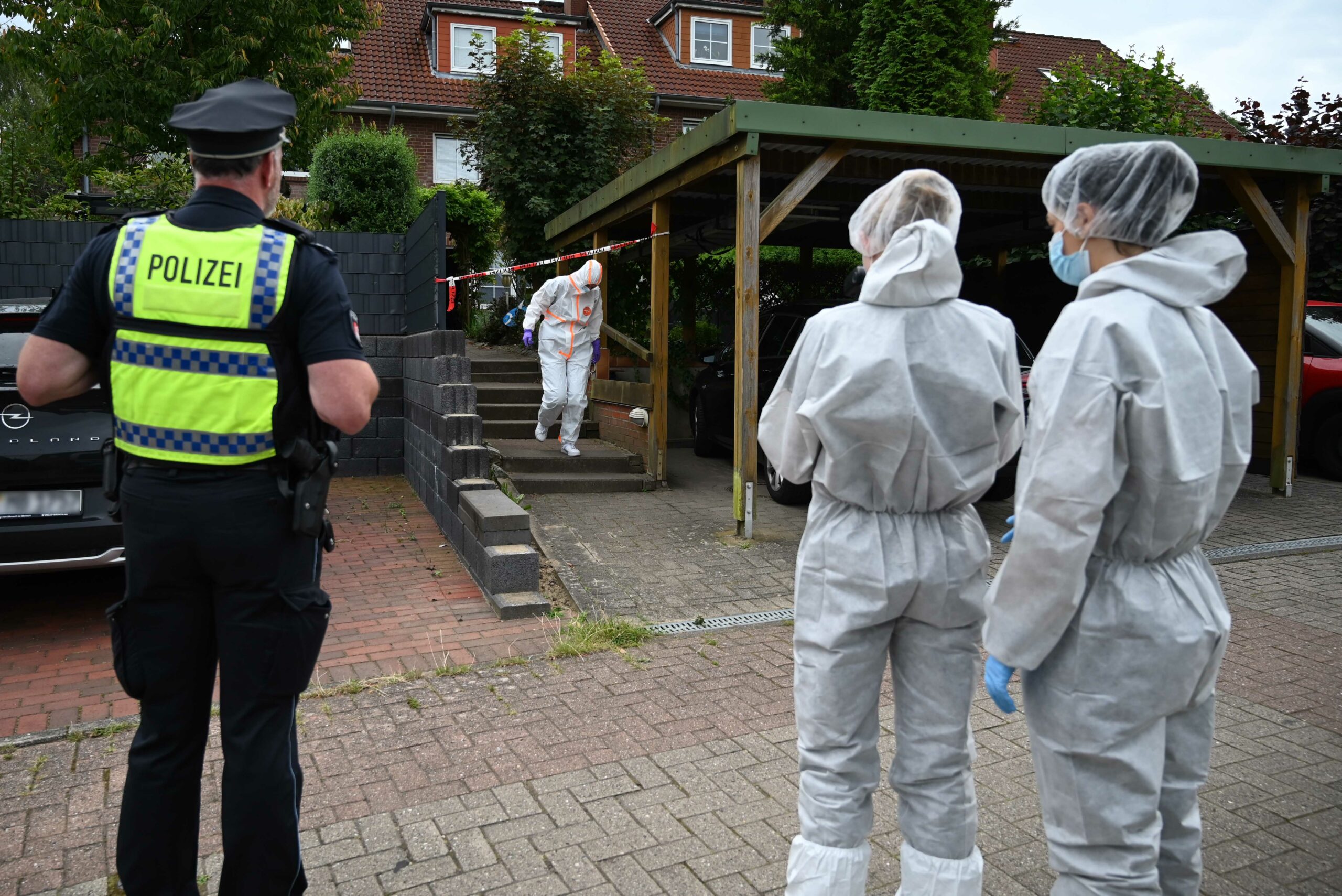 Ermittler in weißen Schutzanzügen stehen vor dem Reihenhaus.