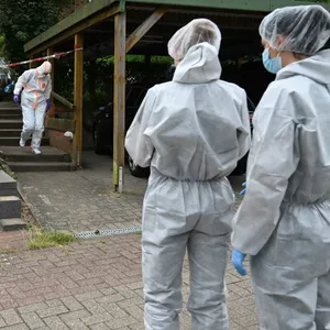 Ermittler in weißen Schutzanzügen stehen vor dem Reihenhaus.