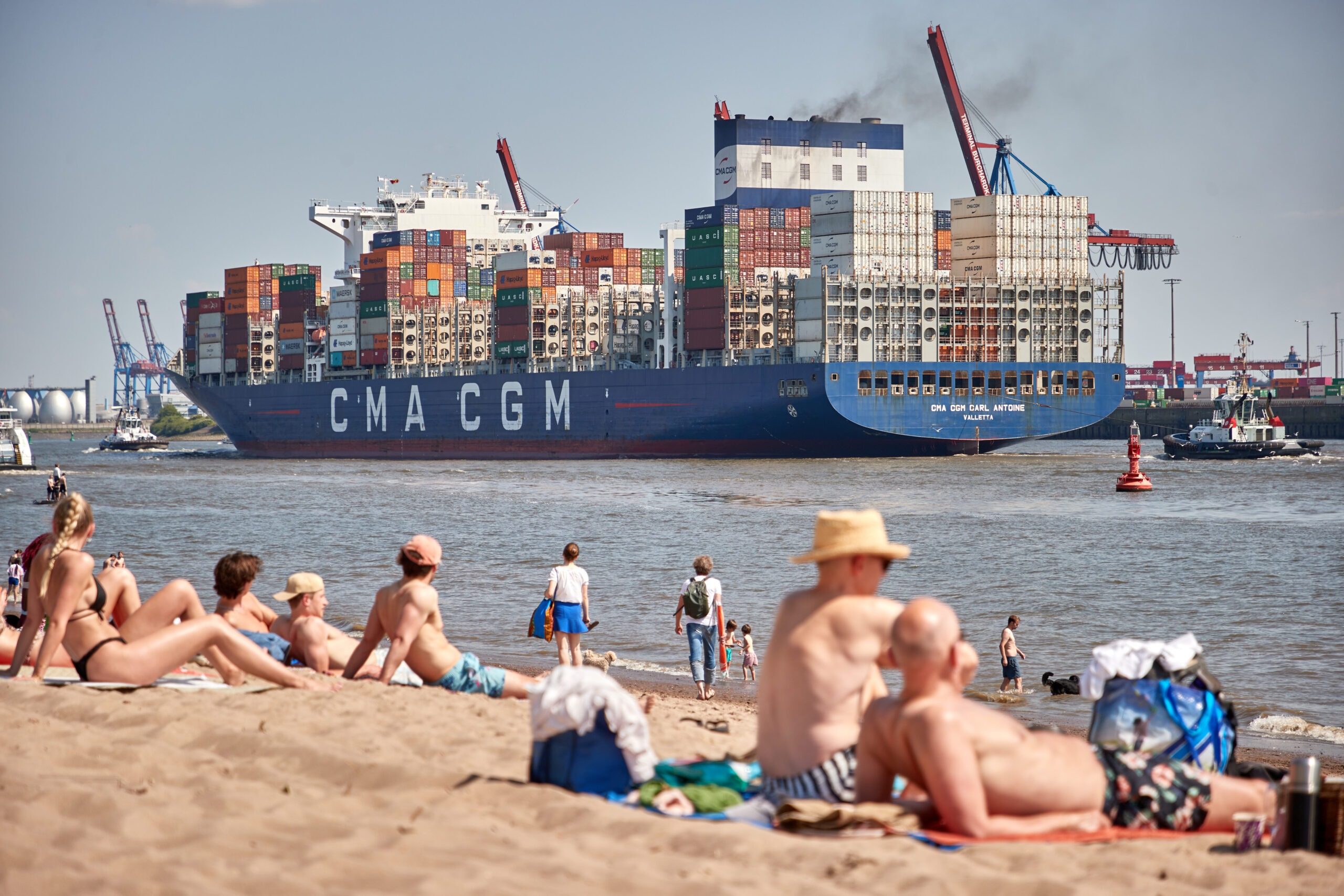 Menscehn am Strand vor Containerschiff