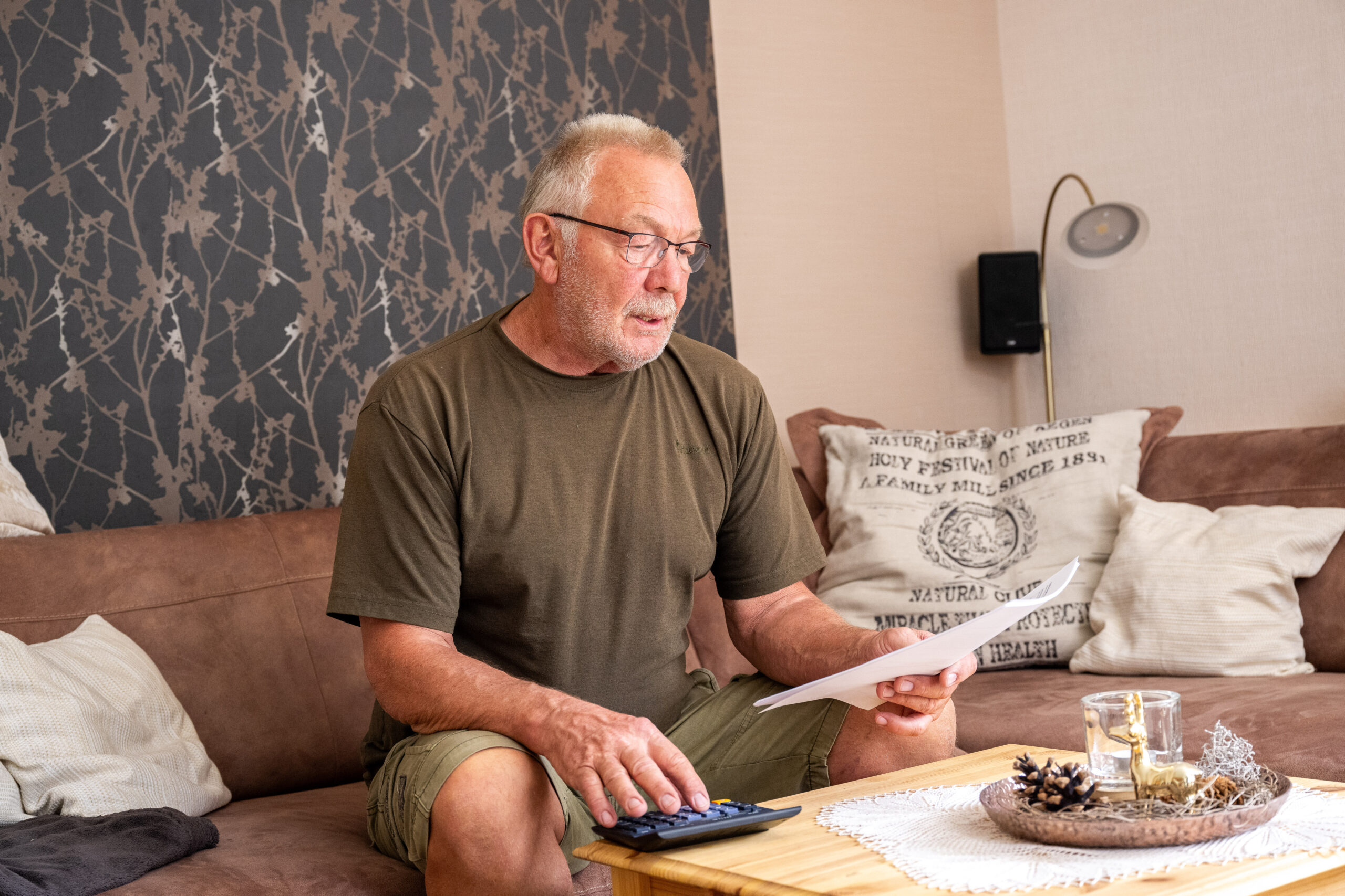 Mann sitzt mit Papier in der Hand auf einem Sofa.