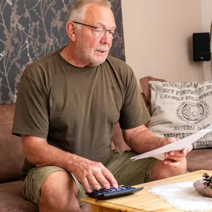 Mann sitzt mit Papier in der Hand auf einem Sofa.