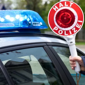 Polizist hält eine Polizeikelle mit Aufschrift Halt Polizei vor ein Polizeiauto mit Blaulicht