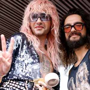 Zwei Männer mit Sonnenbrillen, einer mit rosa Haaren, der andere dunkelhaarig
