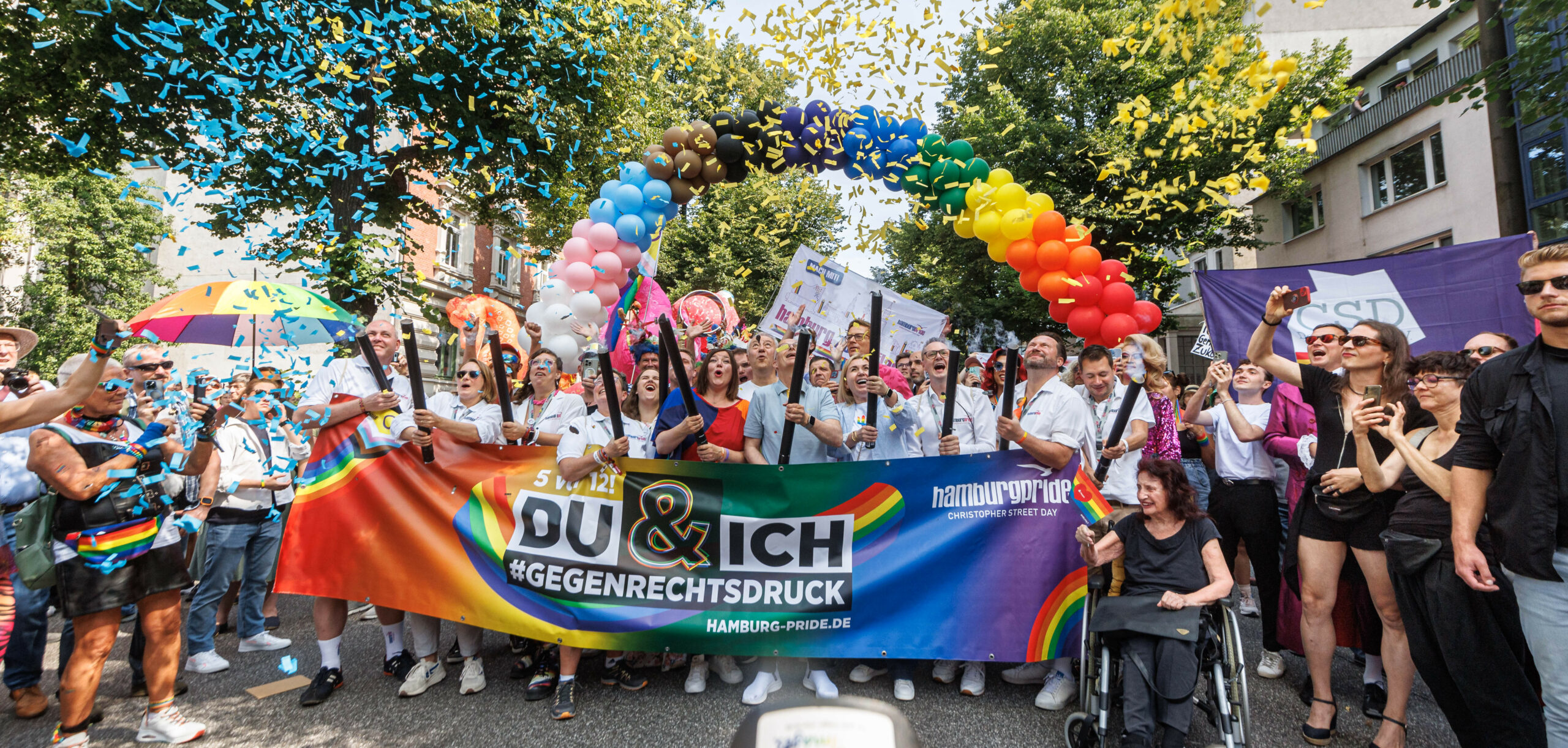 Regenbogen aus Luftballons, Menschen, die Konfetti in die Luft schießen