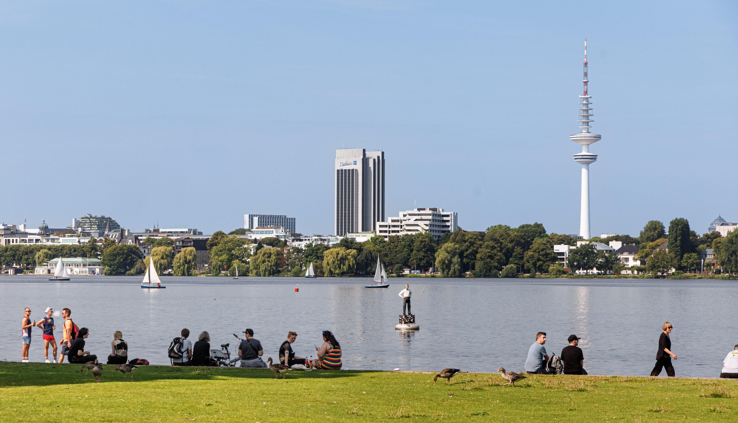 Hamburger sitzen bei blauem Himmel und Sonnenschein am Schwanwiek an der Außenalster.