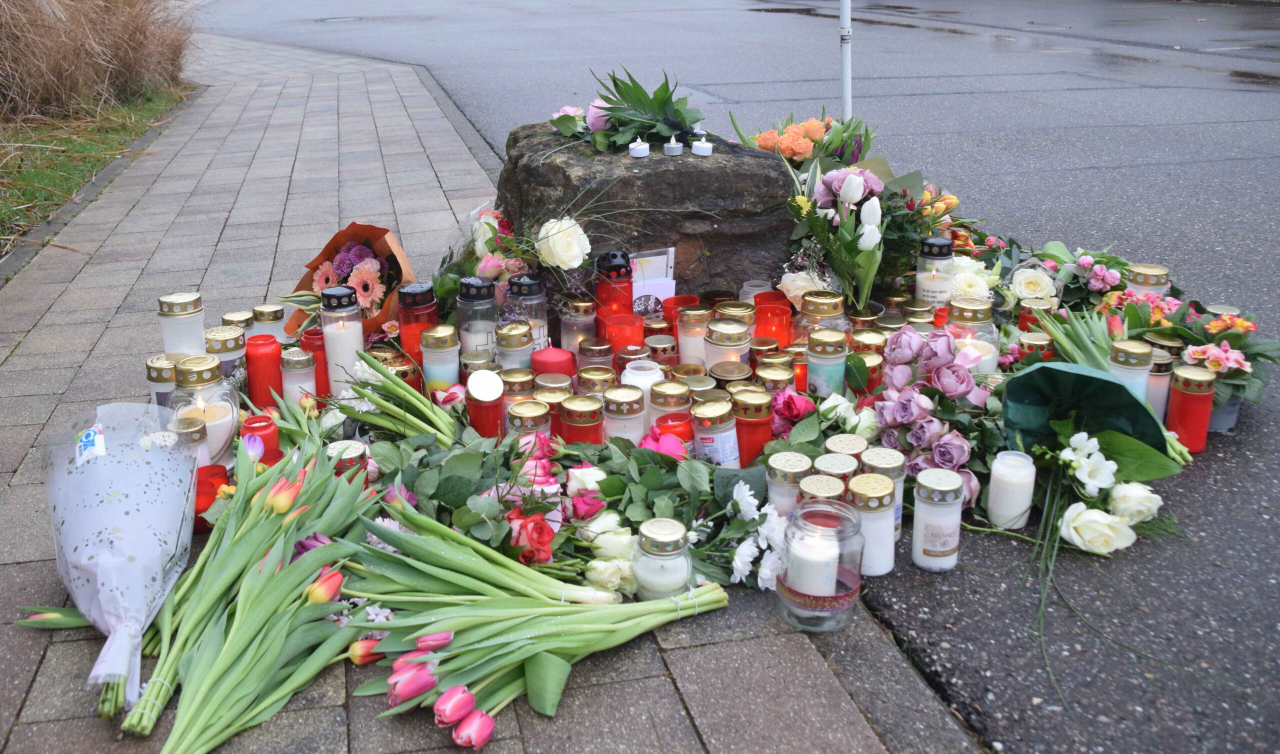 Blumen und Kerzen zum Gedenken an das Opfer liegen vor einer Schule.