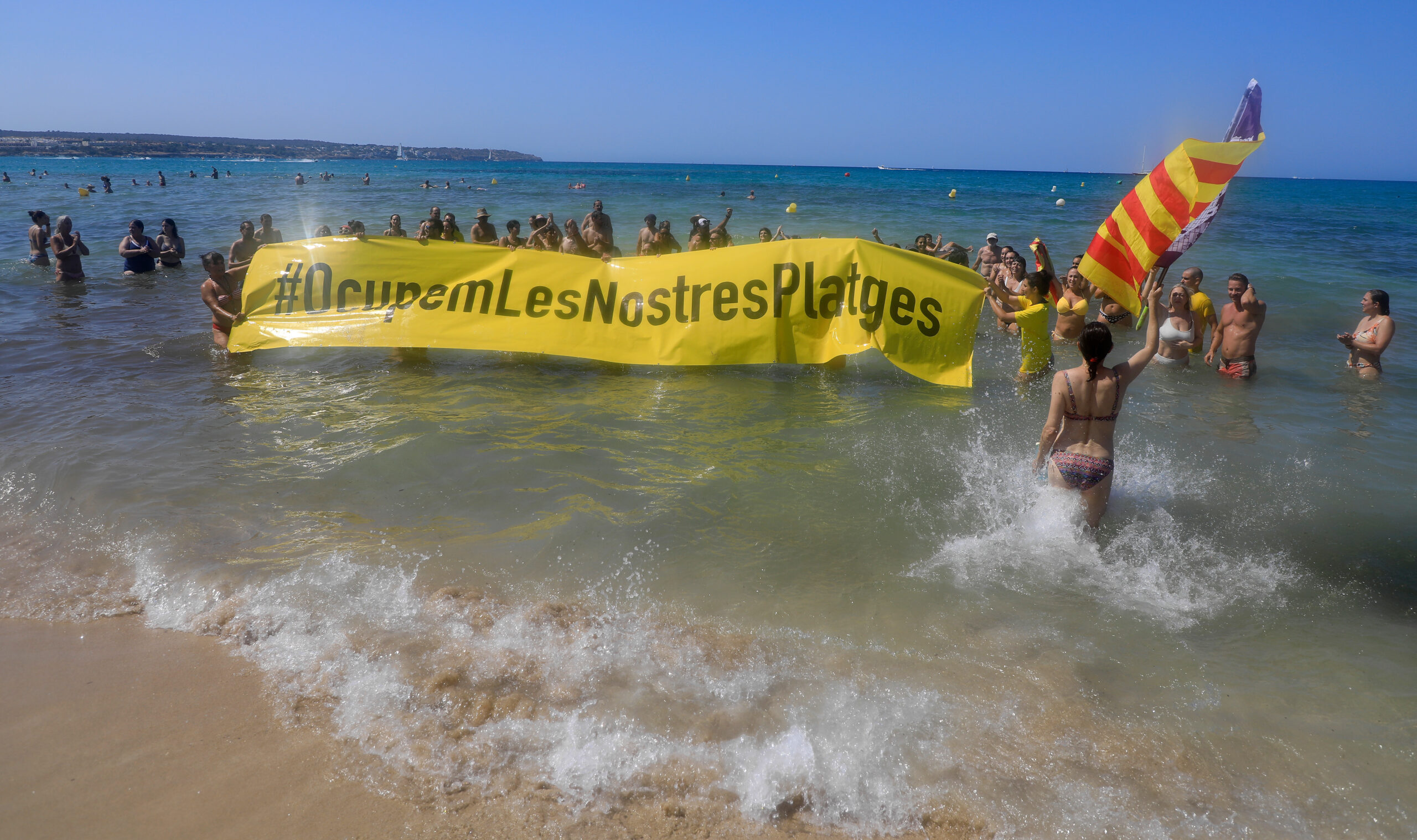 Leute halten an einem Strand auf Mallorca ein Banner "#Sie besetzen unsere Strände" aus Protest gegen den Massentourismus auf der Balearen-Insel.