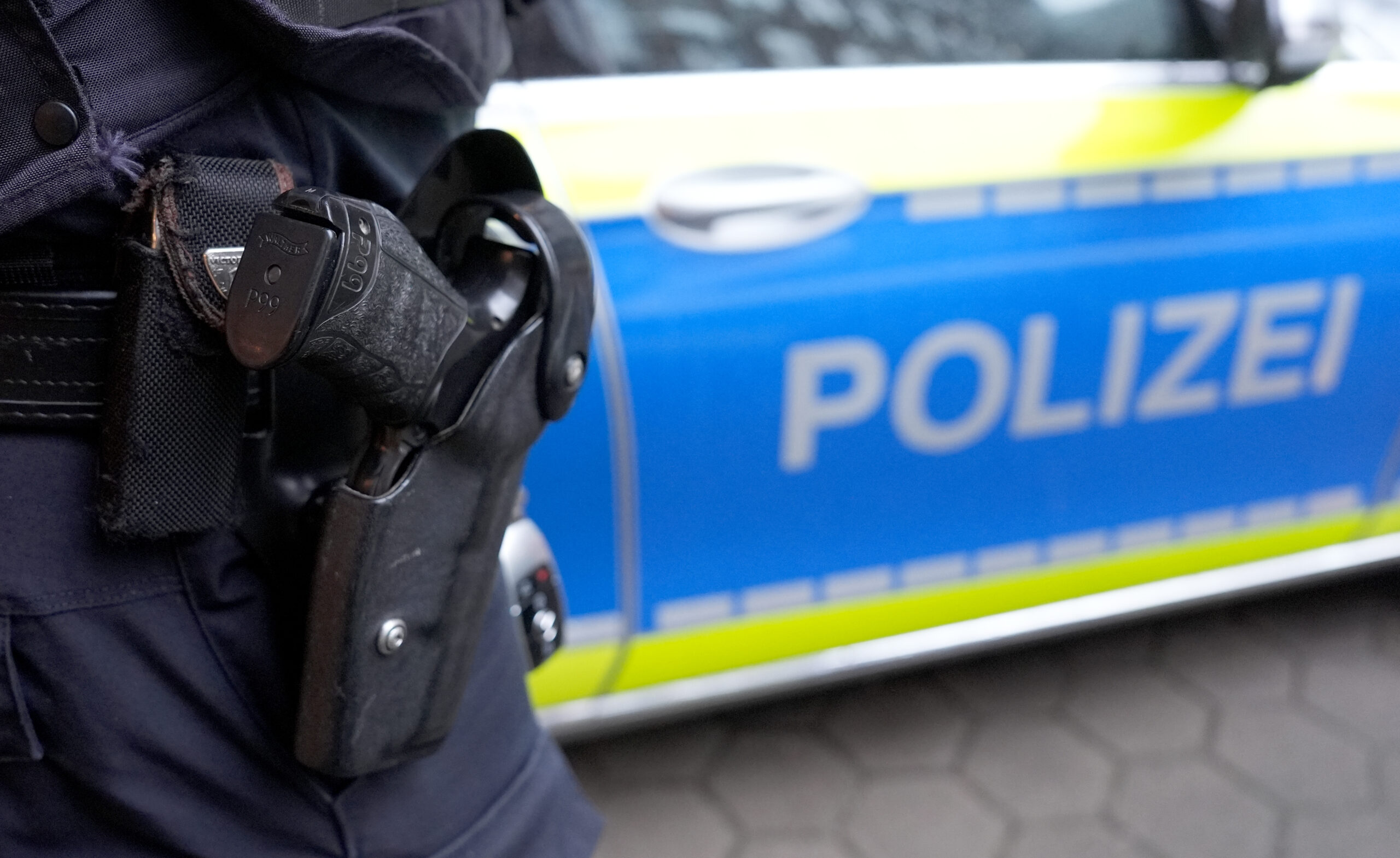 Polizist mit Waffenholster vor Polizeiauto