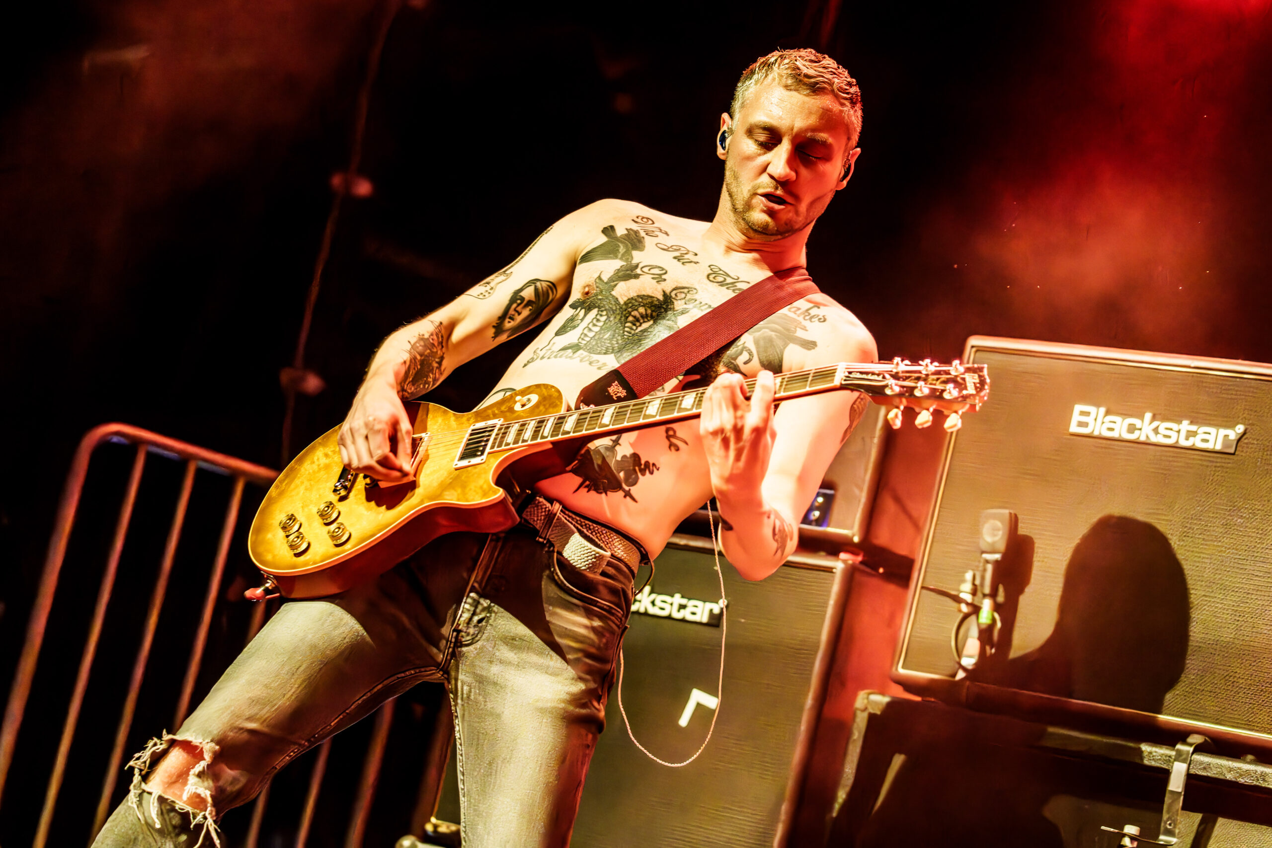 Billy Lunn mit Gitarre auf der Bühne, hinter ihm Boxen, er hat einen nackten Oberkörper