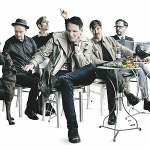 Bandfoto, die fünf Männer sitzen an Cafétischen, ein Hund ist auch im Bild