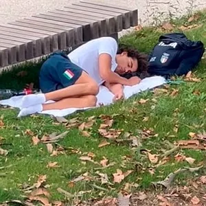 Thomas Ceccon schläft auf einem Handtuch vor einer Parkbank im Olympischen Dorf