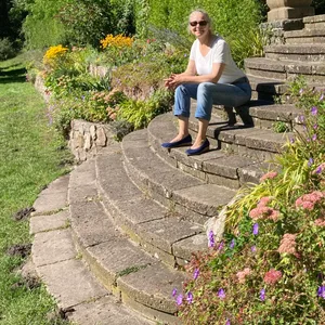 Frau in Jeans und T-Shirt auf einer Freitreppe inmitten von Blumen