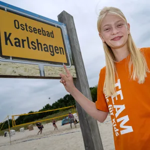 Blondes Mädchen in orangenem Shirt am Strand