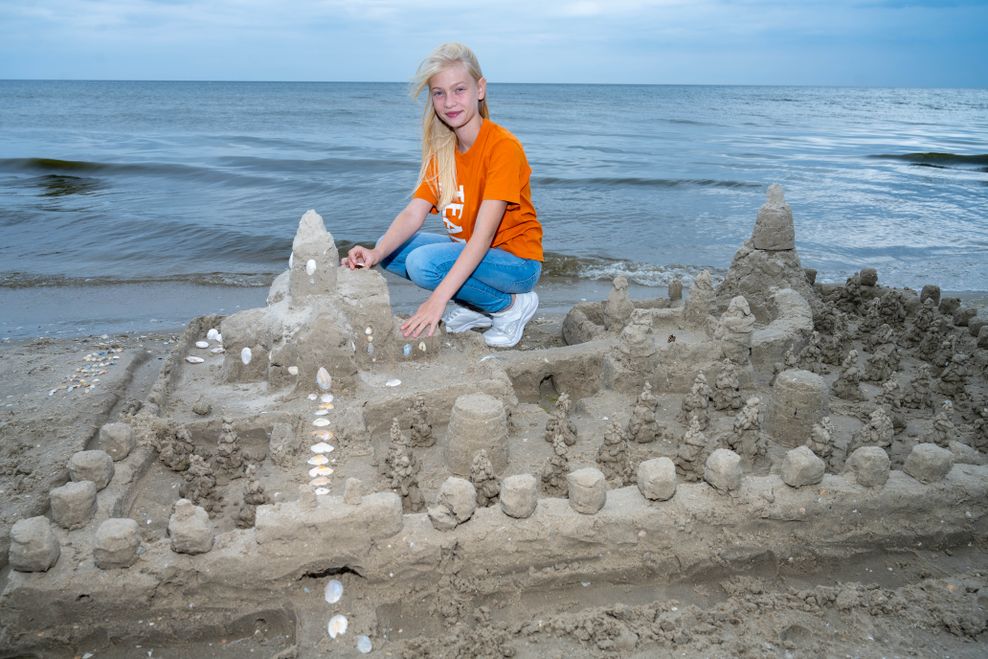 Greta hockt an einer Sandburg am Strand von Usedom.