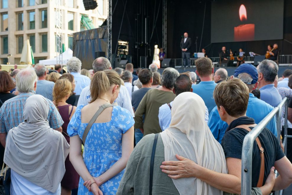 Menschen mit gesenkten Köpfen vor einer Bühne