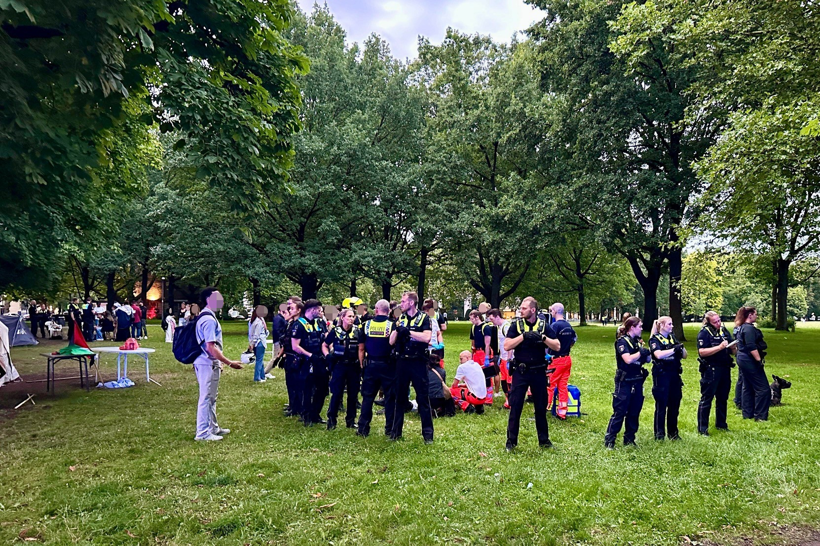 Polizisten schirmen Rettungssanitäter ab, die neben dem Palästina-Camp auf der Moorweide eine Person versorgen.