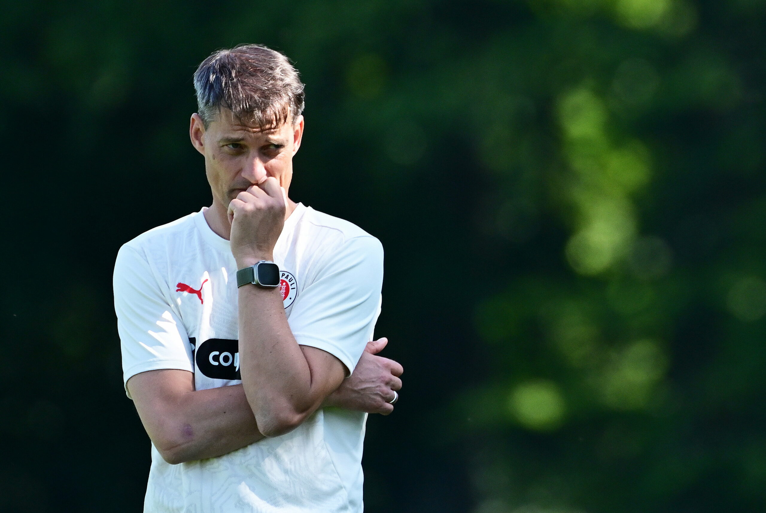 St. Paulis Trainer Alexander Blessin denkt im Training nach, stützt seinen Kopf auf seine Hand.