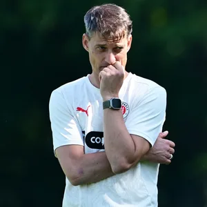 St. Paulis Trainer Alexander Blessin denkt im Training nach, stützt seinen Kopf auf seine Hand.