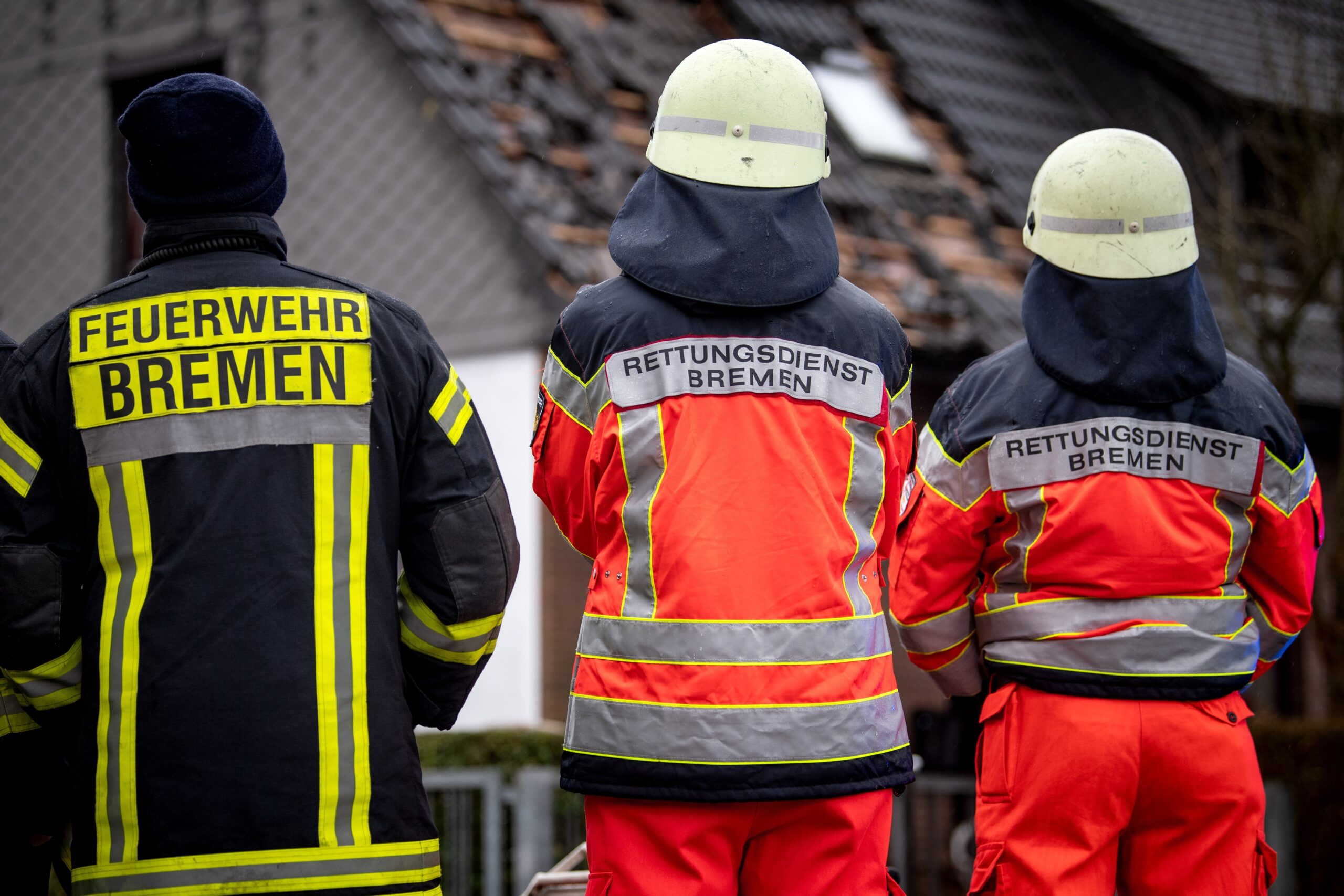 Einsatzkräfte vom Rettungsdienst und der Feuerwehr stehen vor einem ausgebrannten Dachstuhl.