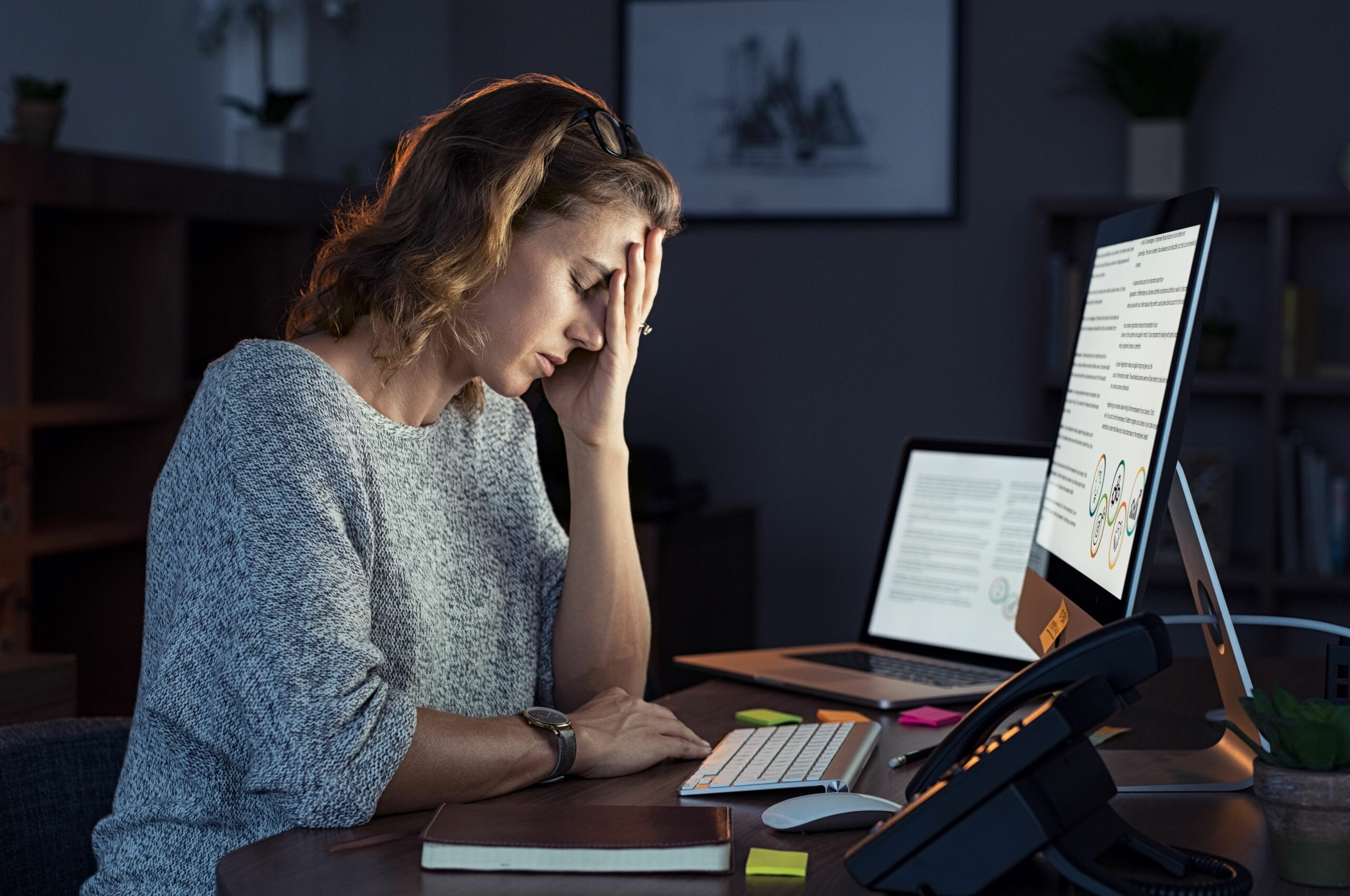 Eine Frau arbeitet an einem Computer, während sie ihren Kopf in ihre Hand stützt.