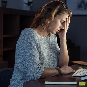 Eine Frau arbeitet an einem Computer, während sie ihren Kopf in ihre Hand stützt.