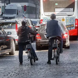 Ein Linienbus, ein Auto und zwei Radfahrer halten vor einer Ampel.