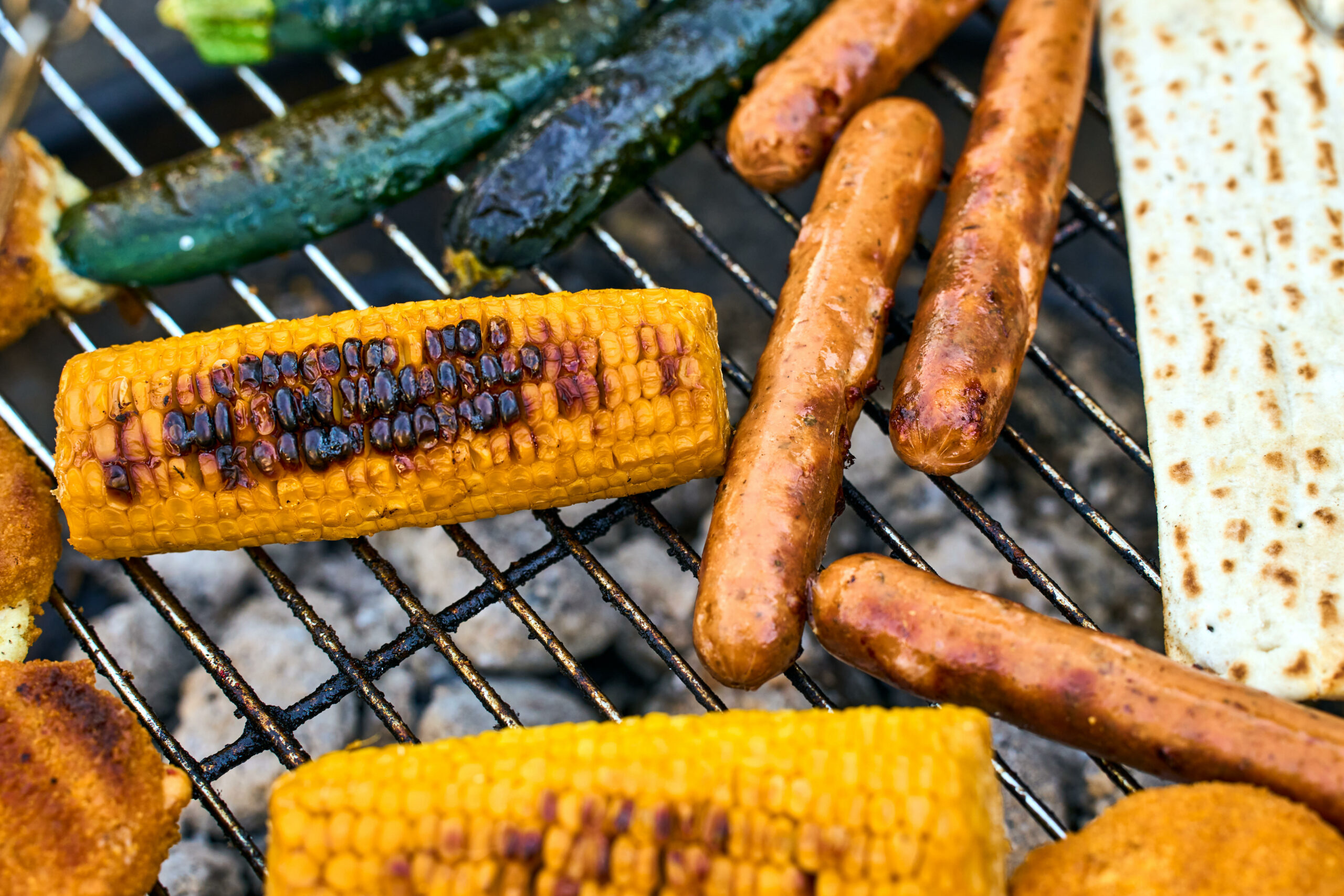 Maiskolben, Würstchen, Gemüsebratlinge und Grillkäse brutzeln auf dem Grillrost bei einer sommerlichen Grillparty