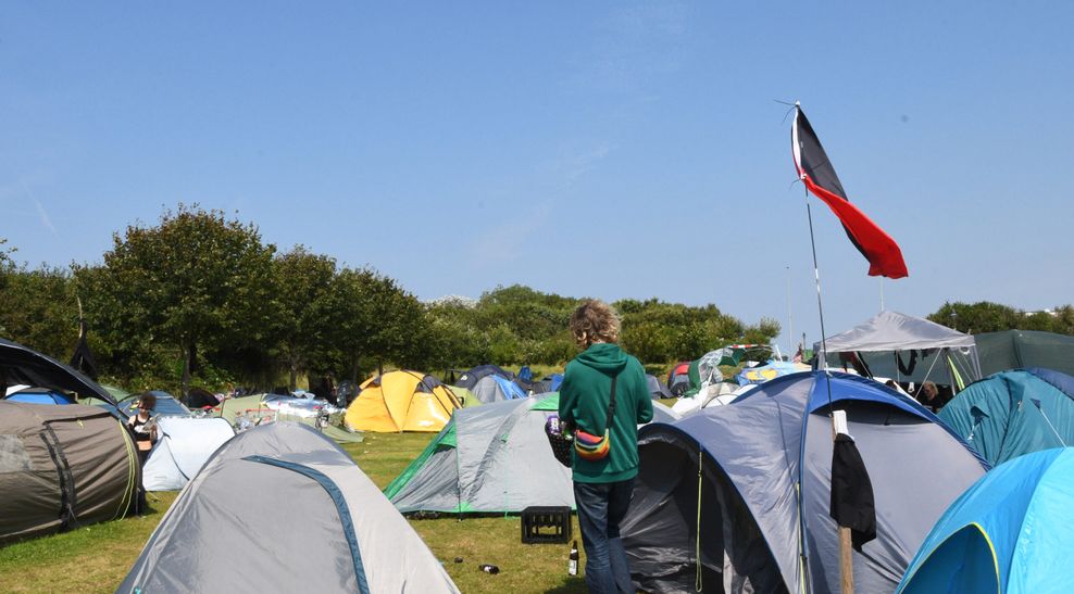 Eine schwarz-rote Flagge einer Antifagruppen weht neben Zelten im Punk-Protestcamp auf der Festwiese. Bis zum 1.9. wollen die Camp-Teilnehmer rund um die Gruppe „Aktion Sylt“ auf der Insel unter anderem für ein solidarisches Miteinander, Klimagerechtigkeit und gegen Gentrifizierung demonstrieren.