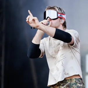 Mann mit Skibrille auf dem Gesicht, er hat ein Mikro in der Hand und rappt oder singt