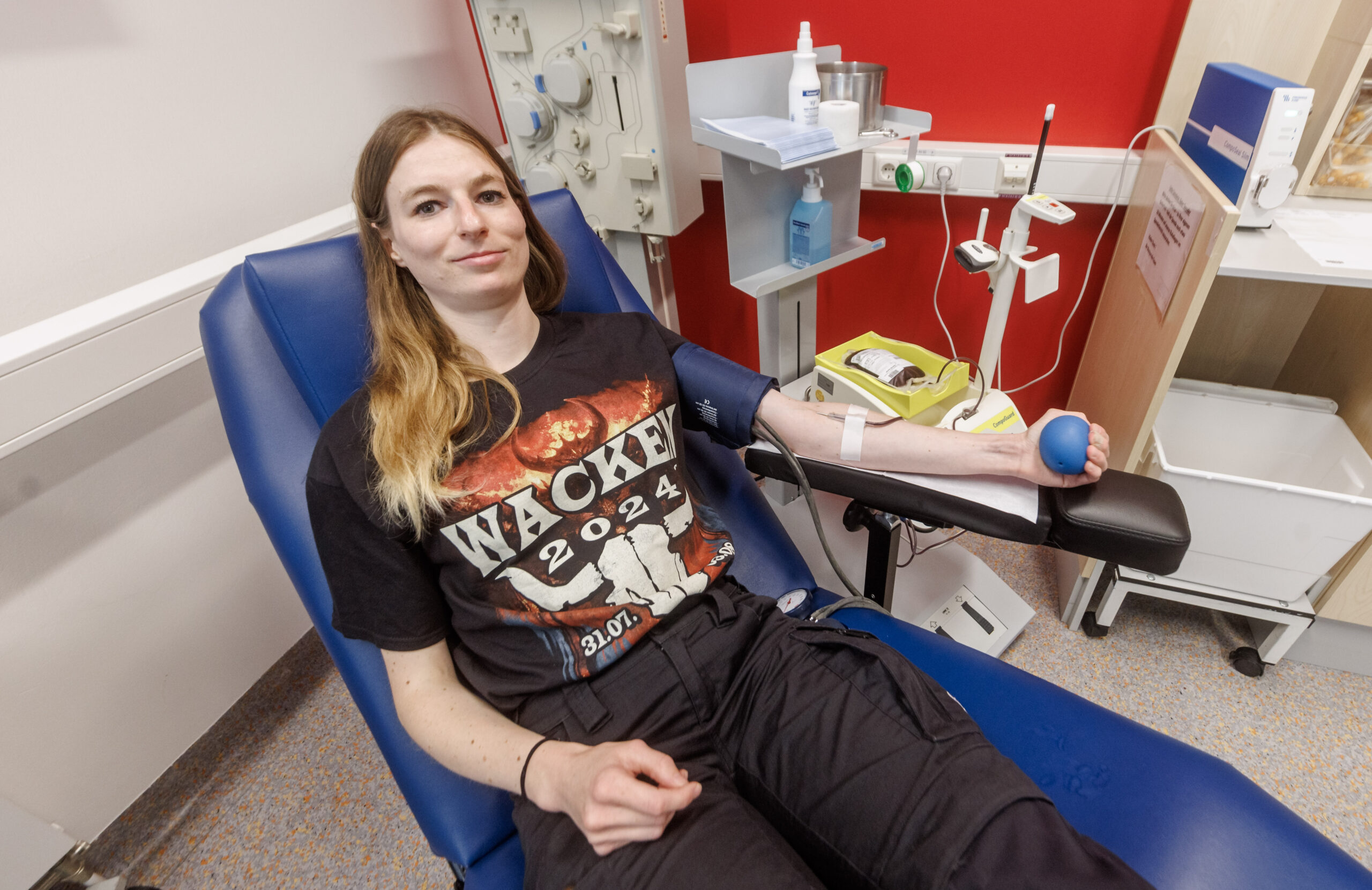 Eine Frau liegt auf einem blauen Stuhl und trägt ein Wacken-T-Shirt während der Blut-Spende.