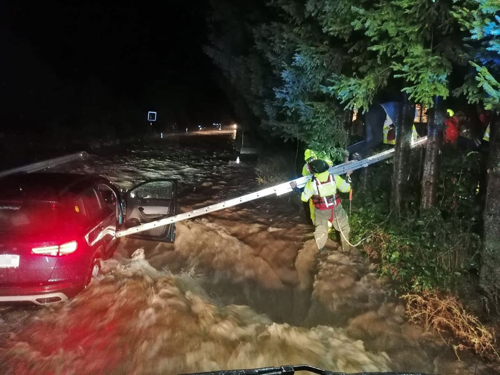 Feuerwehrleute hantieren mit einer Leiter an einem Auto, dass an der zu einem reißenden Strom angeschwollenen Pilach steht.