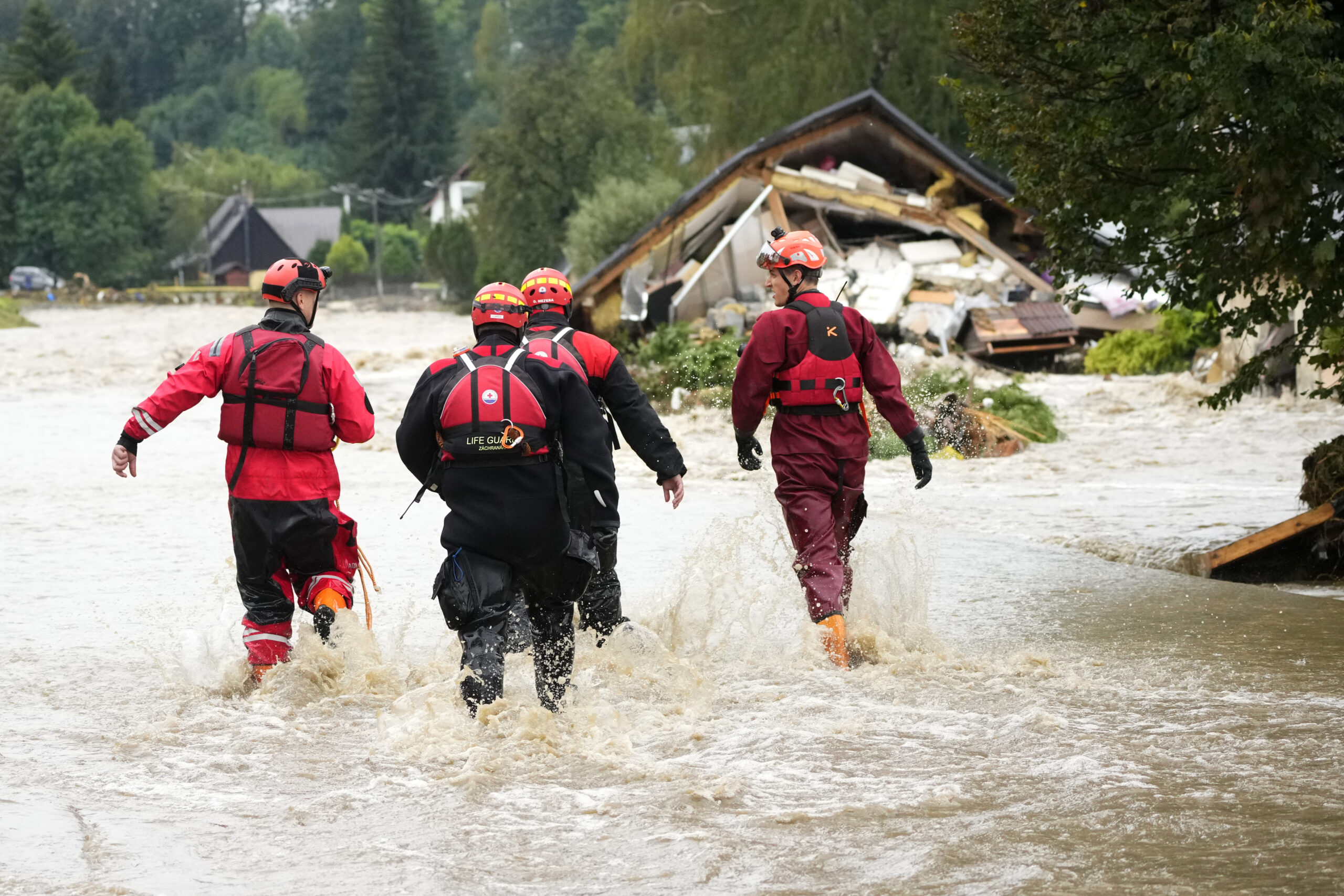 Feuerwehrleute gehen durch eine überflutete Straße.