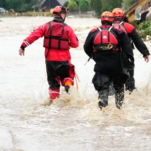 Feuerwehrleute gehen durch eine überflutete Straße.