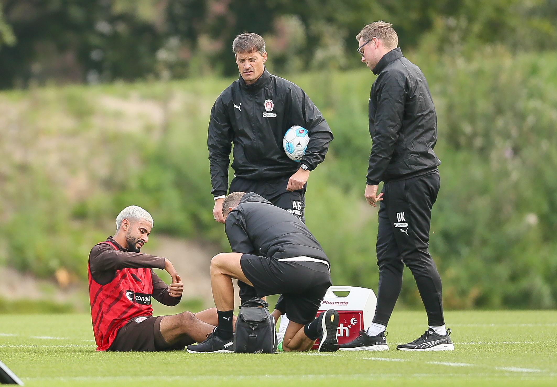 Elias Saad wird von St. Pauli-Physios behandelt und sitzt auf dem Boden.