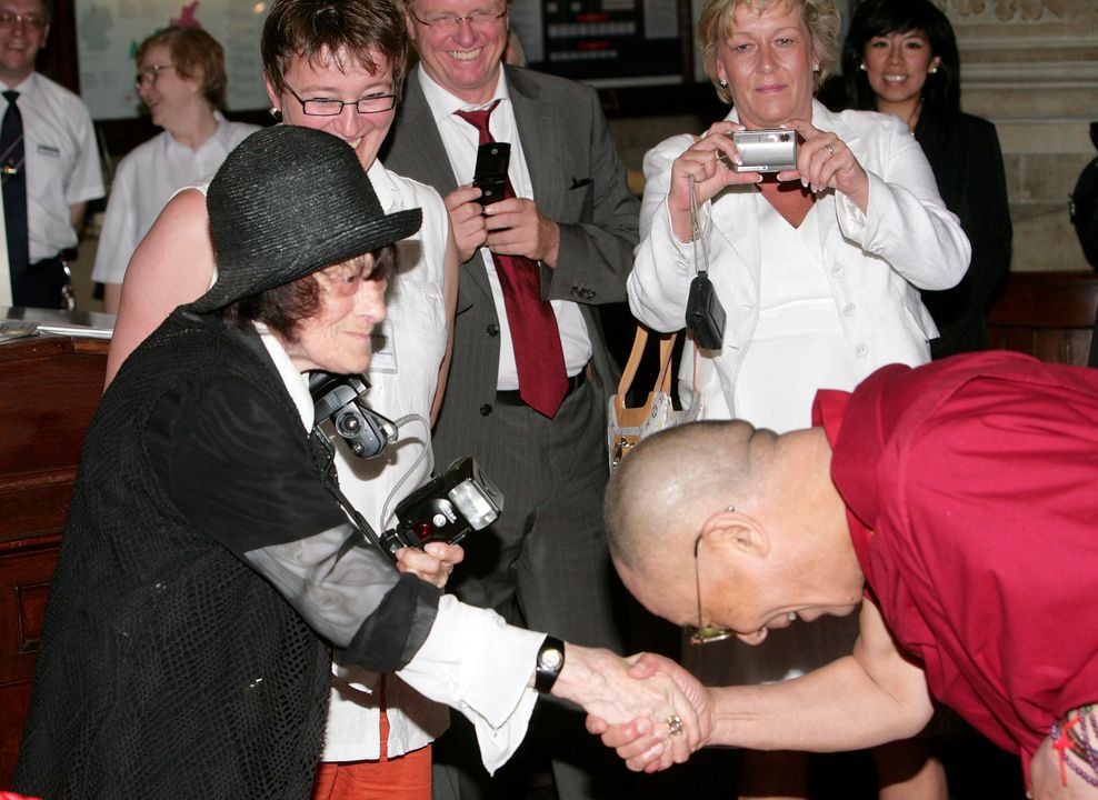 Der Dalai Lama verneigt sich im Hamburger Rathaus vor Erika Krauß, die eine Kamera in der Hand hält.