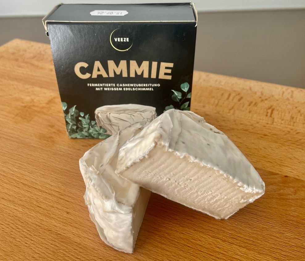 Ein Stück veganer Camembert liegt auf einem Holzbrett.