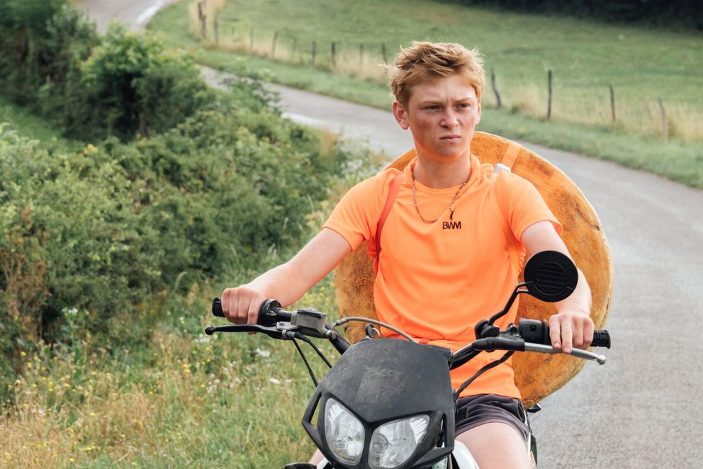 Ein Junge in orangenem T-Shirt fährt auf seinem Motor-Bike.