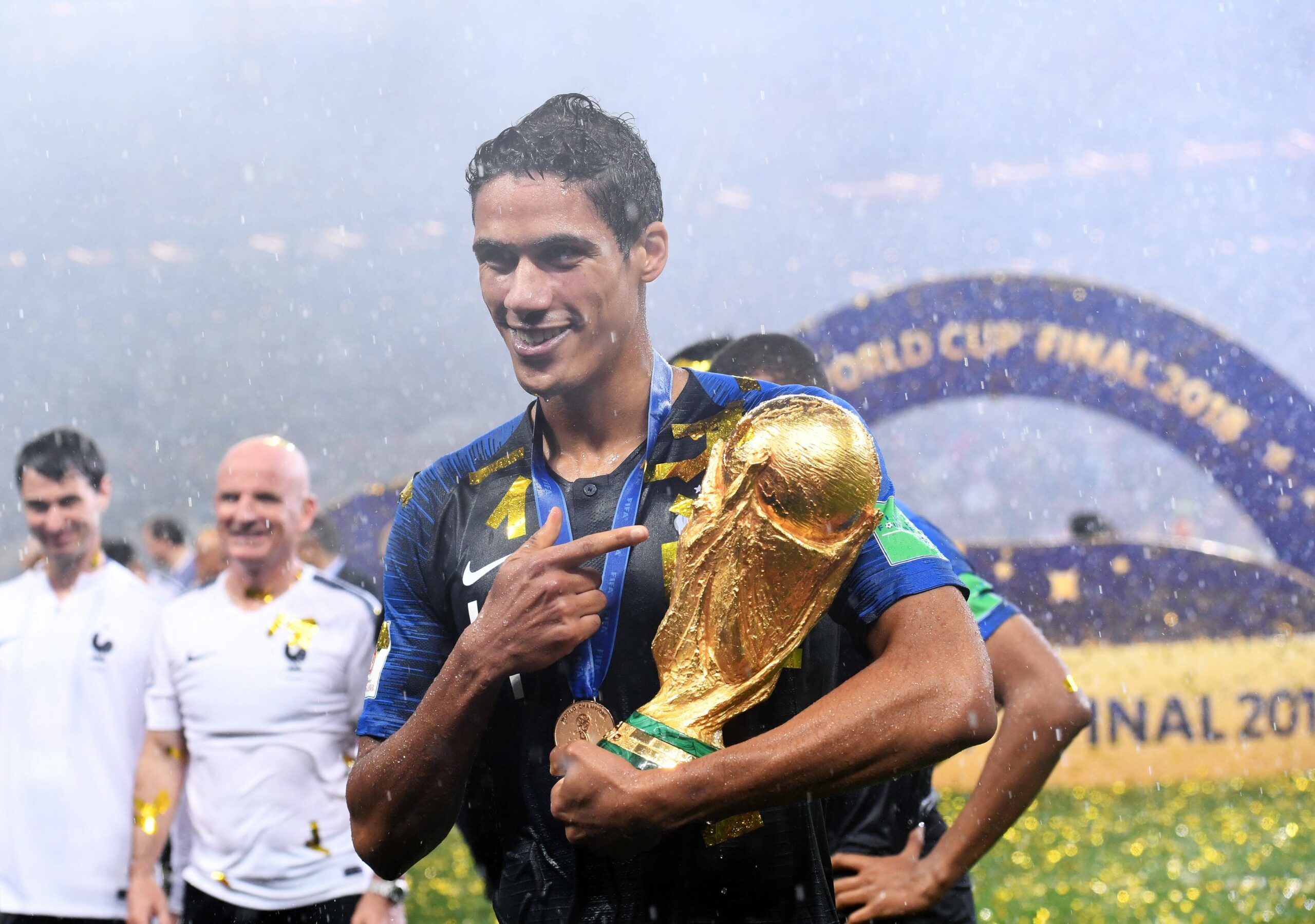 Raphaël Varane zeigt auf den WM-Pokal in seinem Arm.