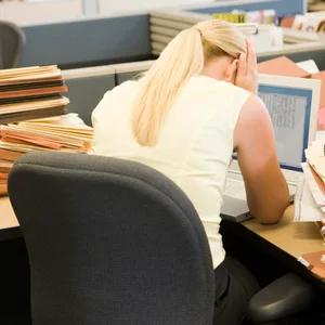 Eine Büroangestelle sitzt verzweifelt über einem Berg an Akten.