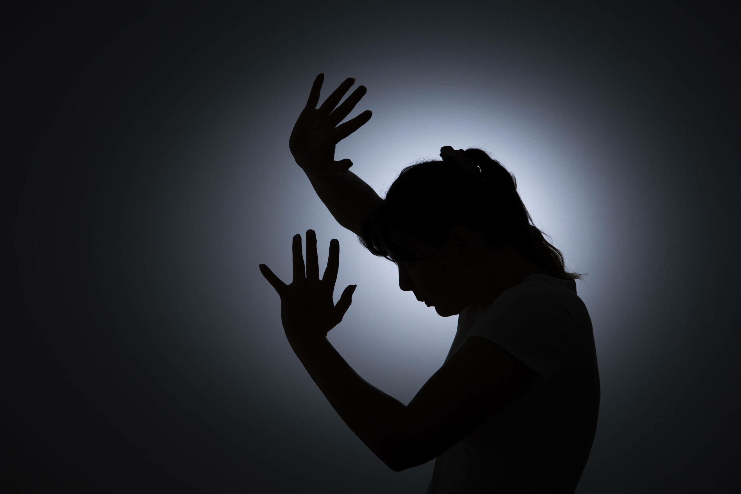 Silhouette einer jungen Frau mit schützenden Händen vor dem Gesicht