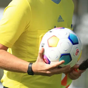 Schiedsrichter trägt einen Fußball vom Platz