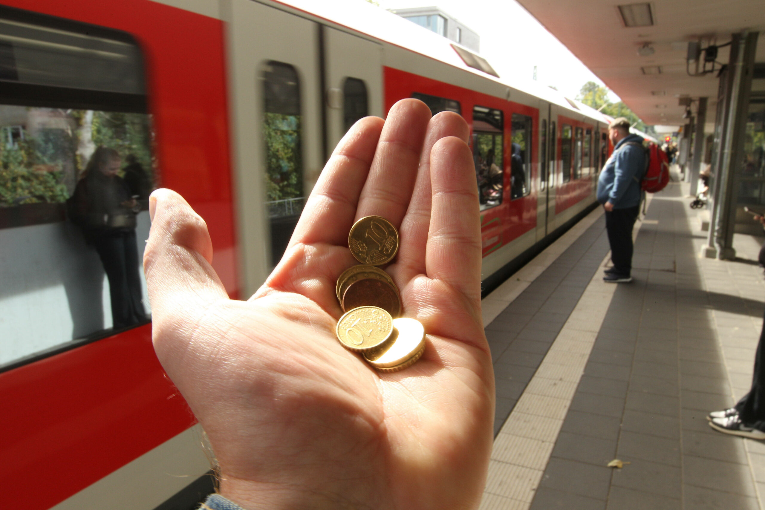 Eine offene Hand mit Geld darin, im Hintergrund eine S-Bahn