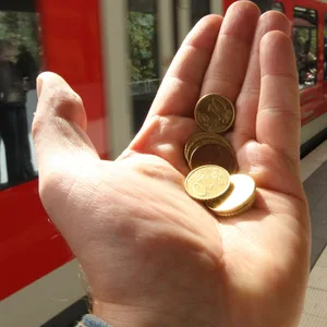 Eine offene Hand mit Geld darin, im Hintergrund eine S-Bahn