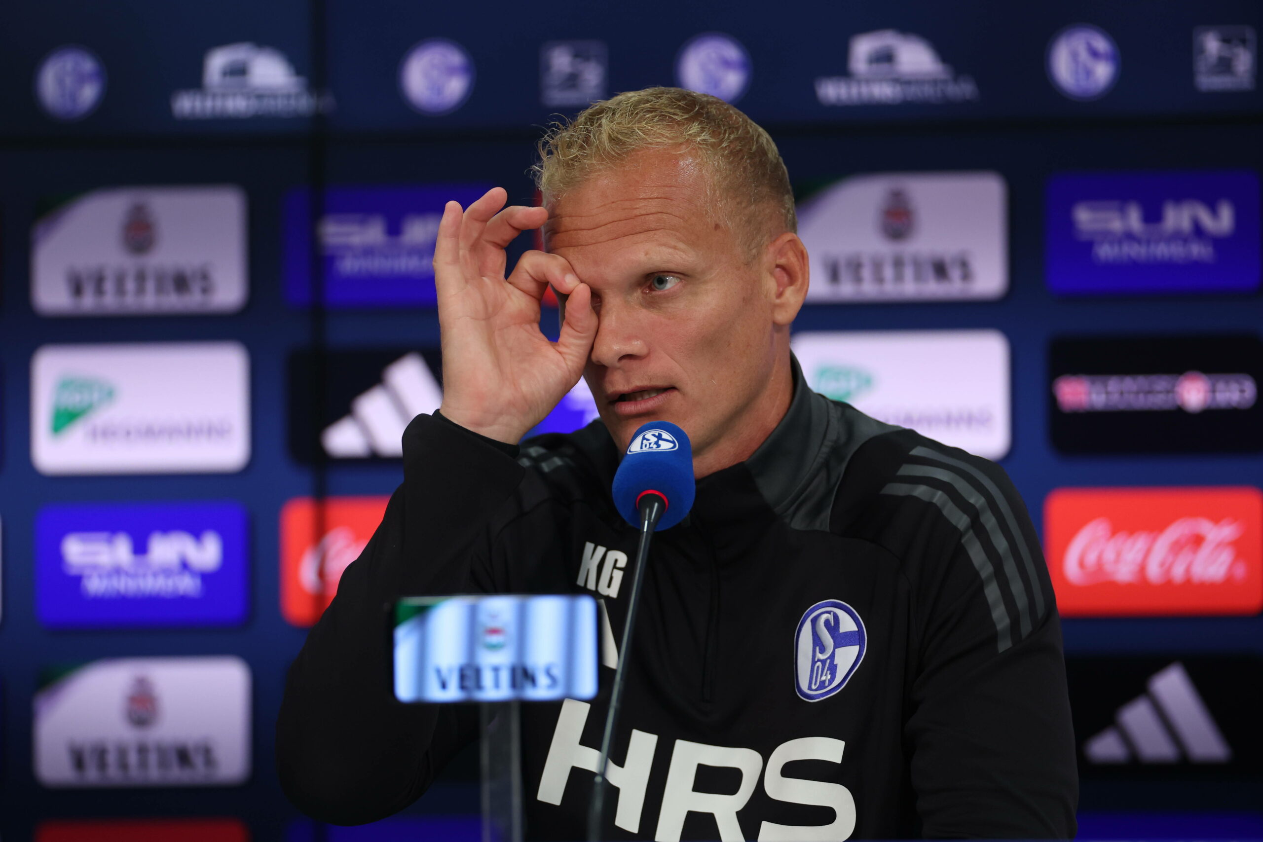 Karel Geraerts auf der Pressekonferenz, formt mit der Hand ein Loch vor sein Auge.