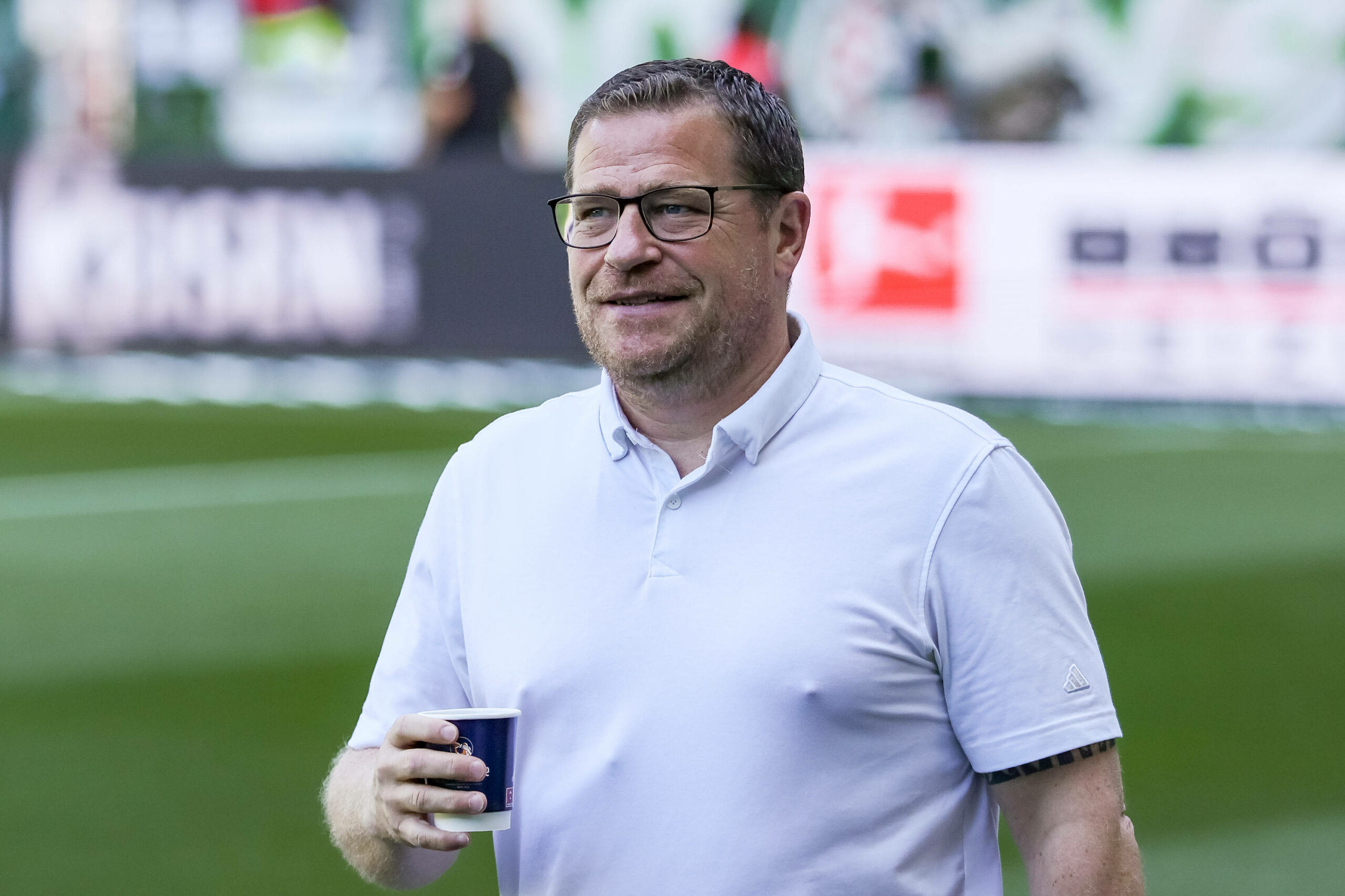 Max Eberl mit einem leichten lächeln und einem Kaffeebecher in der rechten Hand