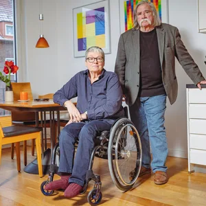 Gerd-Peter Hohaus steht in der Küche von Kerstin Hagemann, die in einem Rollstuhl sitzt.