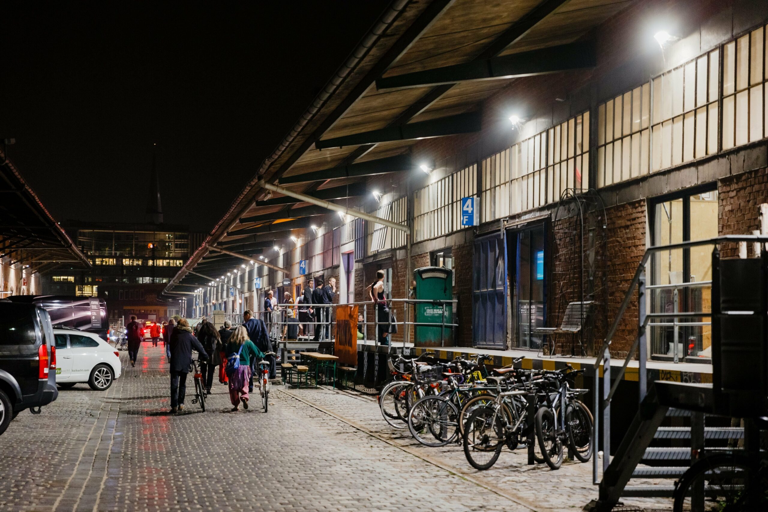 Menschen gehen nachts an einer beleuchteten Lagerhalle vorbei